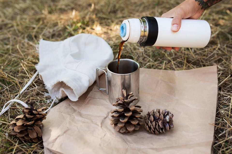 Kaffe hälls från en termos ned i en mugg av rostfritt stål