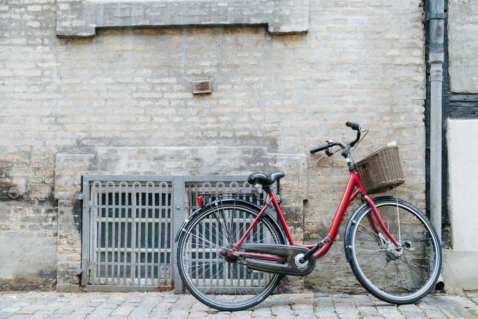 Röd damcykel med korg parkerad vid en vit tegelvägg